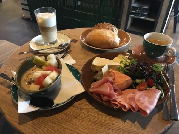 Rustikales Frühstück auf einem kleiner Tisch. Es stehen warme Getränke dabei.